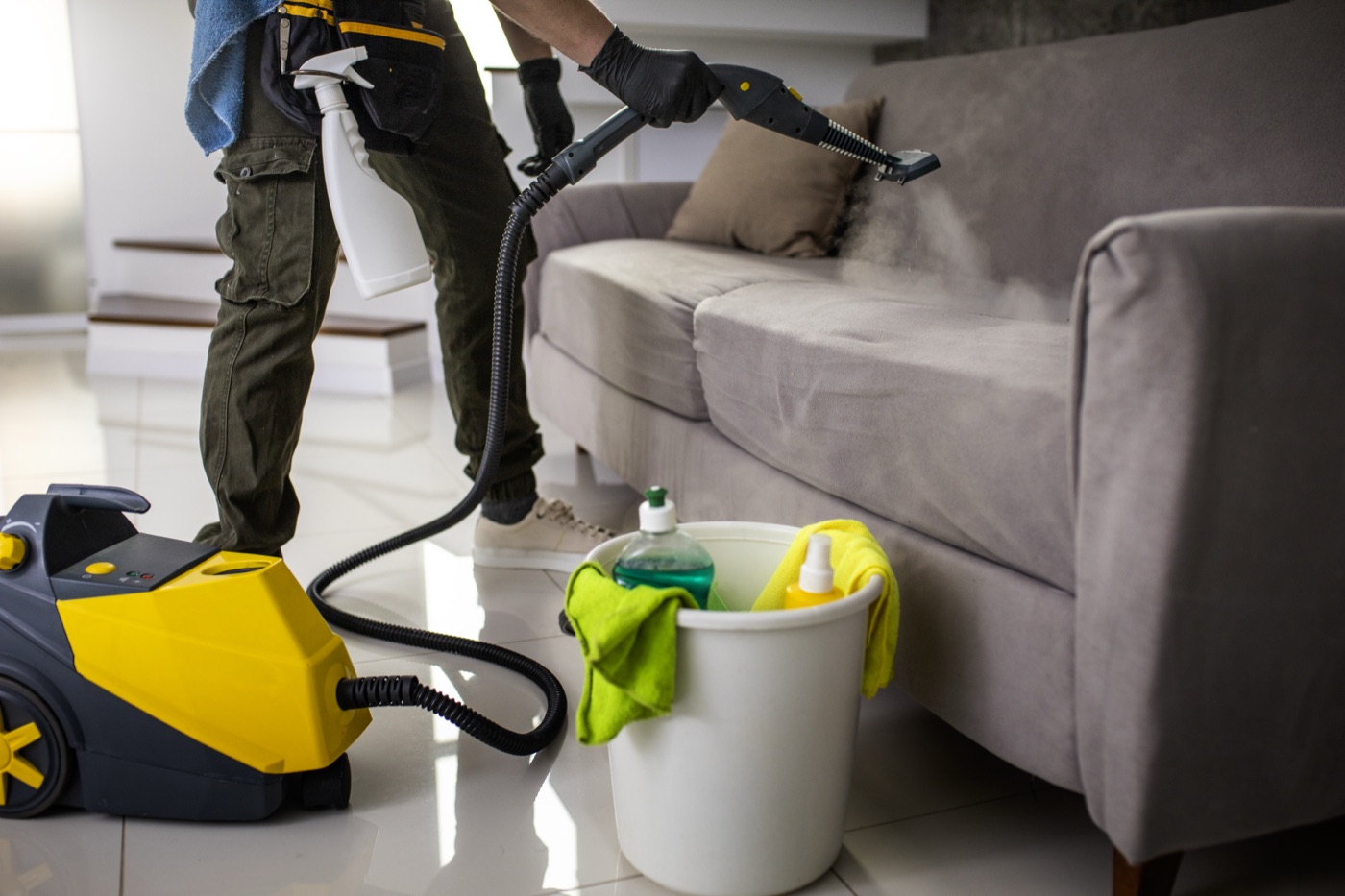 Technician steam-cleaning a fabric sofa with professional equipment